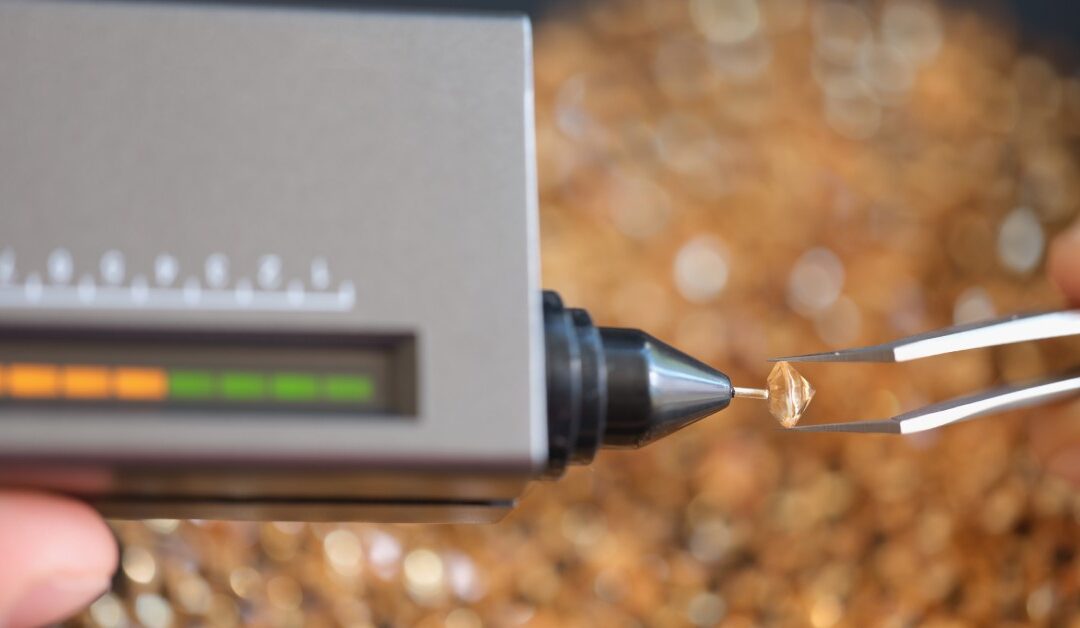A measuring device with a small, fine tip touching a small yellow diamond in between a pair of tweezers.